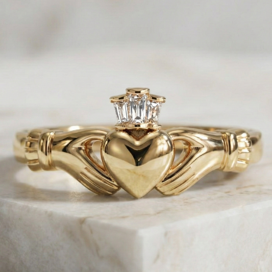 Gold claddagh ring with heart design and diamond on a marble surface