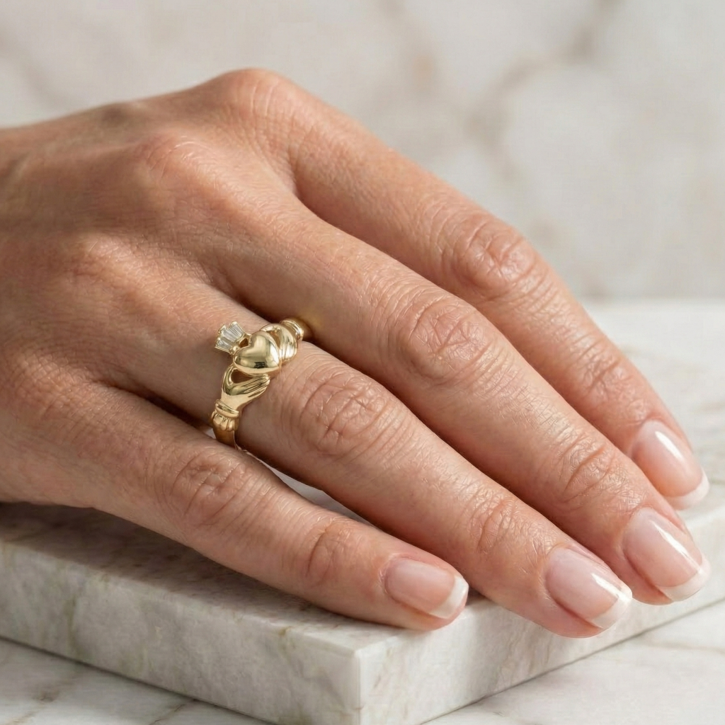 Gold claddagh ring on a person's finger with a marble background