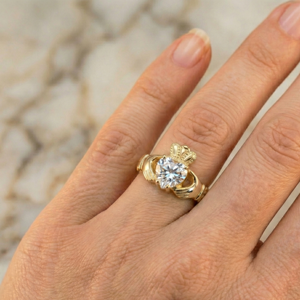 Gold claddagh ring on a person's finger against a neutral background