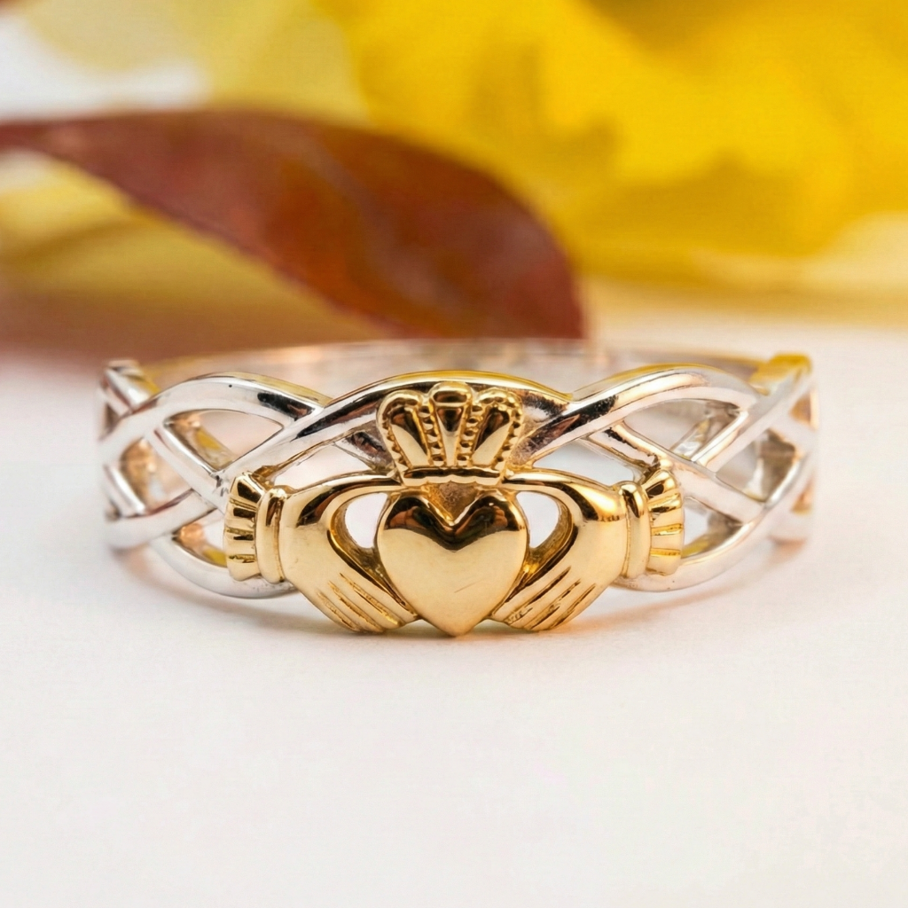 Gold and silver Claddagh ring on a white surface with a blurred yellow background