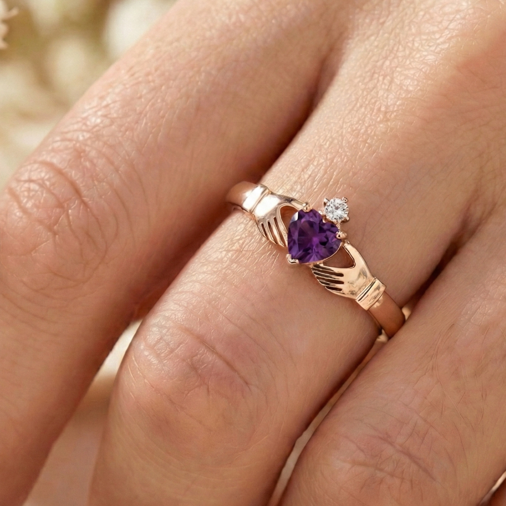 Rose gold claddagh ring with purple heart-shaped gemstone on a finger