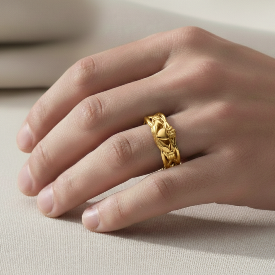 Gold claddagh ring on a person's finger against a neutral background