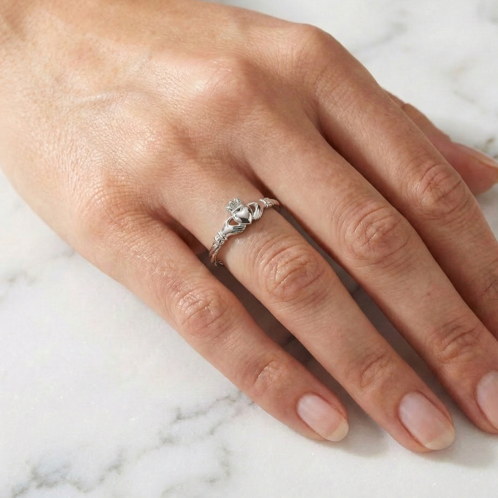 white gold claddagh ring on a person's finger against a marble background