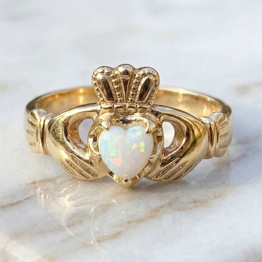 Gold claddagh ring with a heart-shaped opal stone on a marble surface