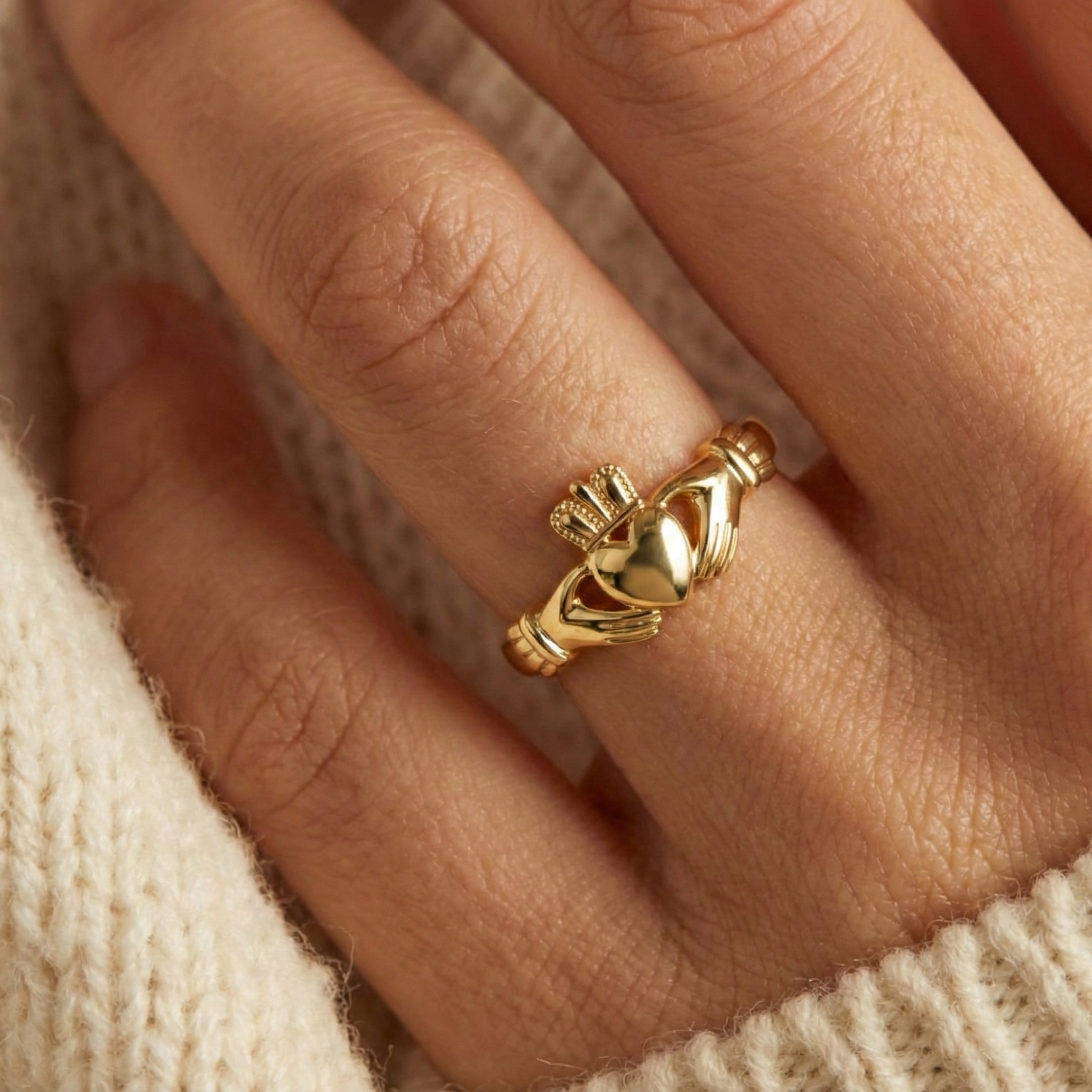 Gold Claddagh ring on a finger with a soft beige background