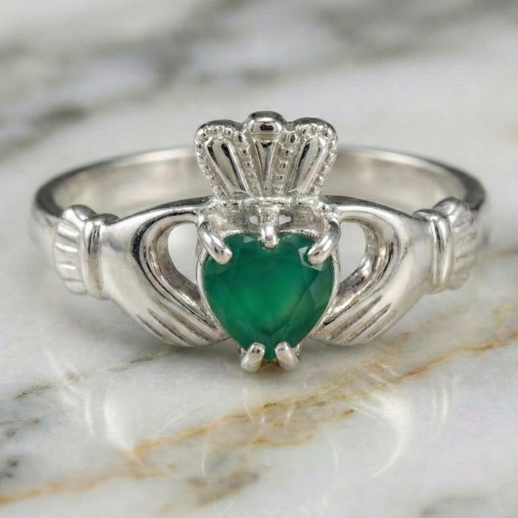 Silver Claddagh ring with a green heart stone on a marble background