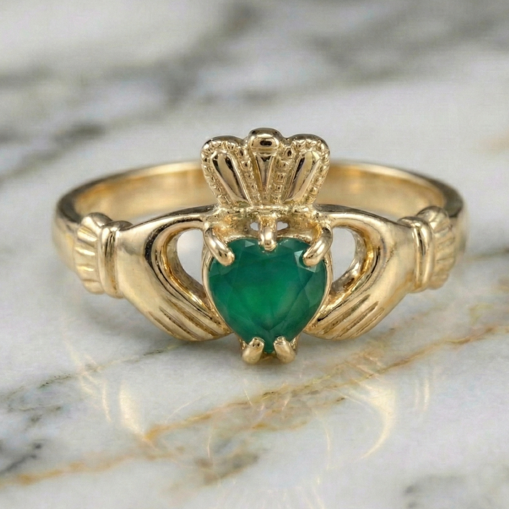 Gold claddagh ring with a green gemstone on a marble surface