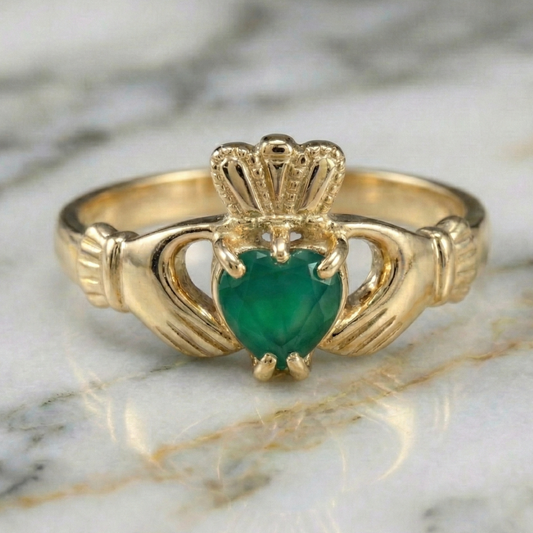 Gold claddagh ring with a green gemstone on a marble surface