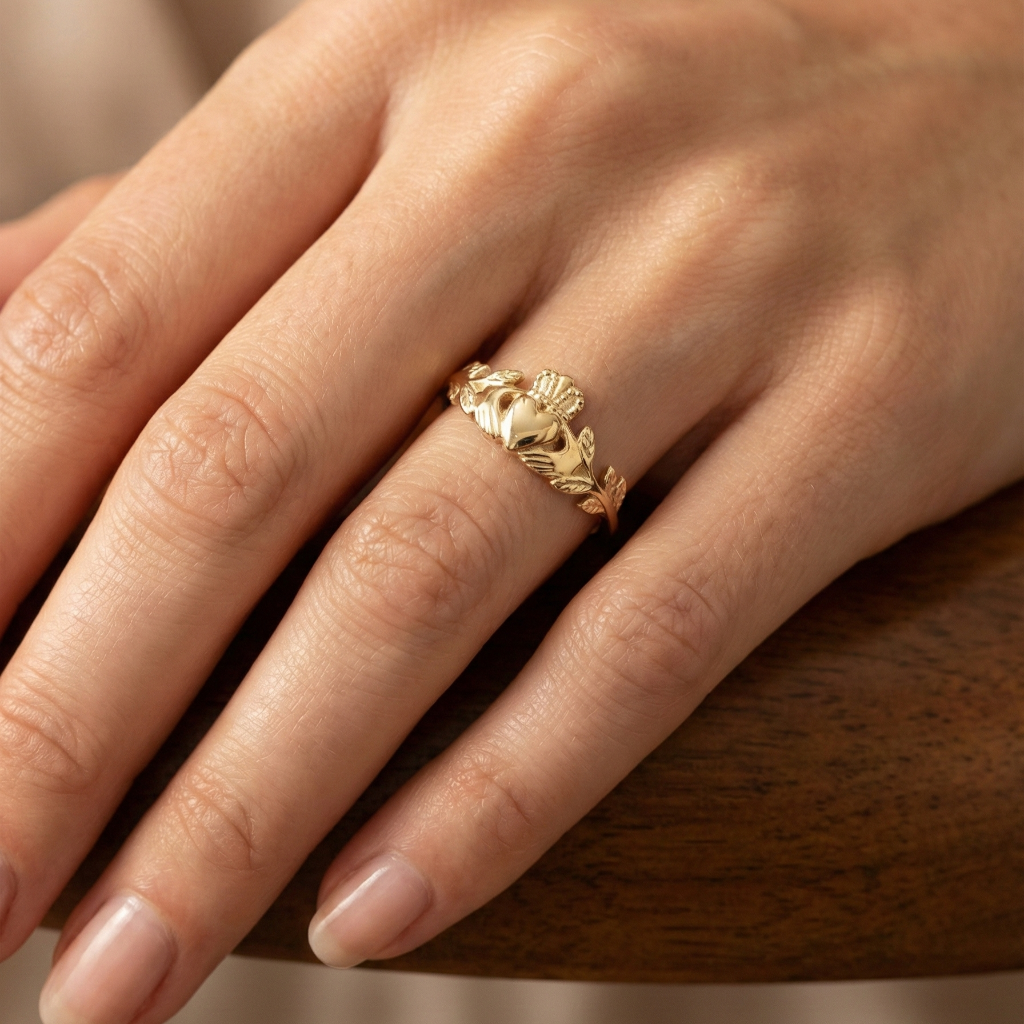 Gold claddagh ring with leaf design on a person's finger against a neutral background
