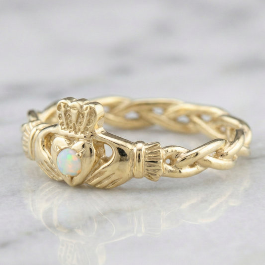 Gold ring with a claddagh design and opal stone on a marble surface