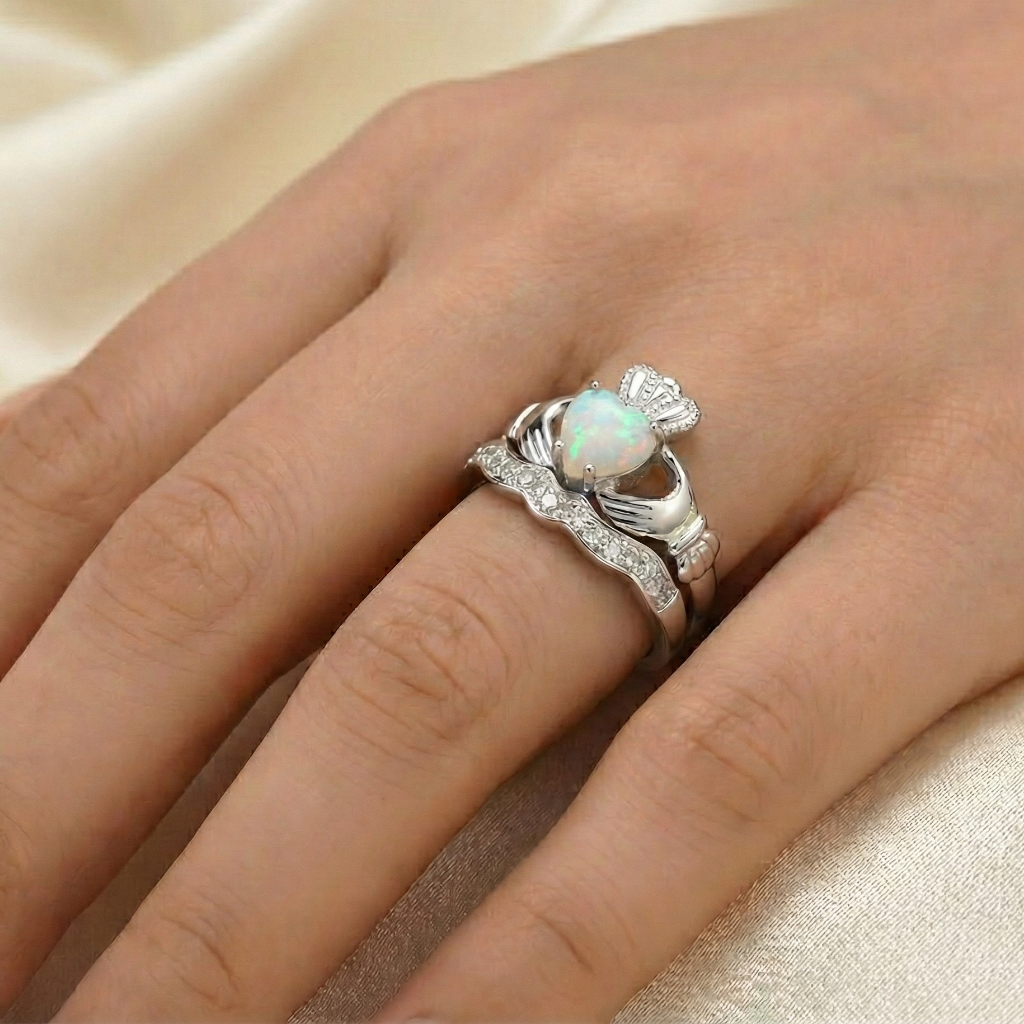 Silver cladadgh ring with an opal stone on a hand against a beige fabric background
